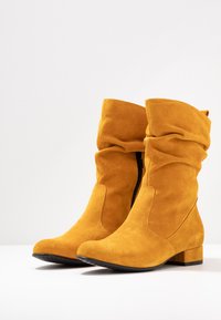 Bottines en daim jaune moutarde avec un design froissé, fermeture éclair et un petit talon. Surface texturée et bout rond.
