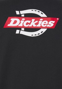 Camiseta de algodón negra con un gran logo gráfico en rojo y blanco. El diseño incluye líneas curvas y un motivo de herradura.