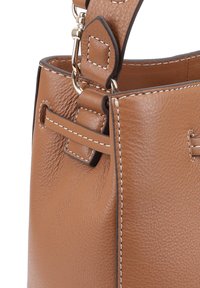 Sac à main en cuir marron avec une finition texturée, présentant des coutures blanches, une bandoulière amovible et des accents en métal.