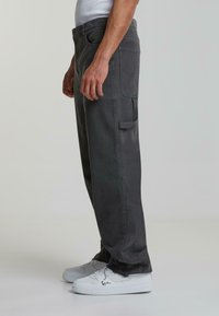 Mørkegrå cargo-bukser laget av robust bomull, med en avslappet passform, sidelommer og synlige sømmer. Brukt med hvite sneakers.