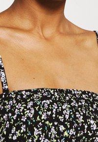 Svart blommönstrad smocktop med tunna axelremmar, dekorerad med små vita, gröna och rosa blommor på texturerad tyg.