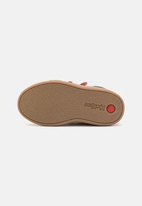 Sole delle calzature in gomma con superficie testurizzata. Presenta un accento circolare rosso e un logo del marchio in rilievo. Il colore è marrone chiaro.