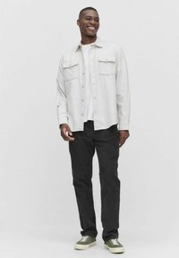 Lysfarvet skjorte med knapper over en hvid T-shirt, parret med sorte bukser og grønne sneakers. Har to brystlommer og en afslappet pasform.