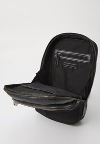 Zaino nero dalla forma arrotondata, con esterno in tessuto e pelle, zip argentata e una tasca interna con zip e dettaglio del logo.