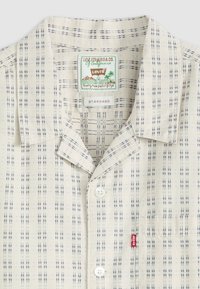 Lichtbeige button-up shirt met een marineblauw geruit patroon. Korte kraag, voorzak met een rode Levi's label, gemaakt van zacht materiaal.