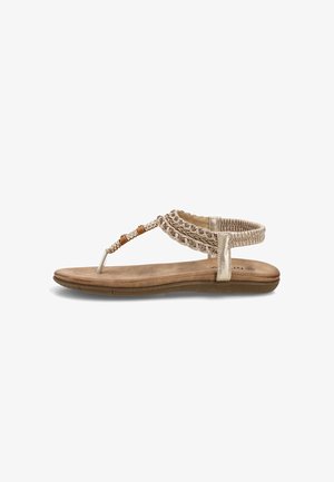 Sandalia plana beige con tiras trenzadas, tira en T con cuentas y banda elástica en el tobillo para un ajuste seguro, sobre fondo blanco.