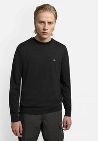 Maglione nero a maglia con scollatura a girocollo e polsini a costine. Presenta un piccolo dettaglio emblematico sul petto. Il tessuto appare liscio.