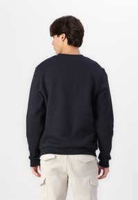 Sudadera azul marino de manga larga y puños acanalados, con cuello redondo y corte relajado. Combinada con pantalones cargo de color claro.