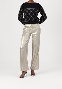 Pull noir en maille avec un motif géométrique et des accents argentés, associé à un pantalon larges jambes argenté brillant et des sandales noires à talons.