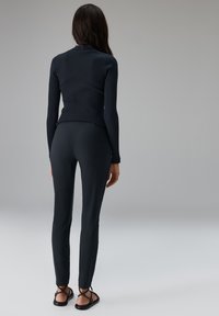 Marineblaues, geripptes Langarmoberteil kombiniert mit enganliegenden marineblauen Leggings und flachen, schwarzen Riemchensandalen. Glatte Textur, minimalistisches Design.