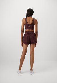 Bordeauxfarbenes Sport-BH mit dünnen Trägern und Cutout-Detail, kombiniert mit passenden hochgeschnittenen Shorts. Glattes Material mit lockerer Passform.