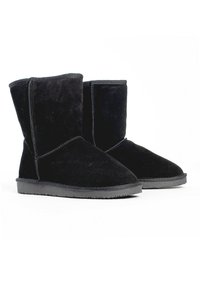 Botines de ante negro con una textura suave, punta redondeada y suela de goma plana. Presentan costuras laterales y un caña corta y recta.