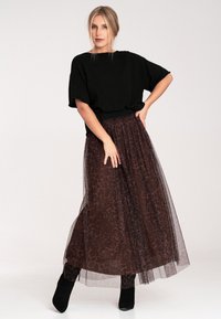 Czarny, oversize sweter połączony z półprzezroczystą, brązową spódnicą w panterkę z tiulu, z lekko opadającą sylwetką i botkami do kostek.