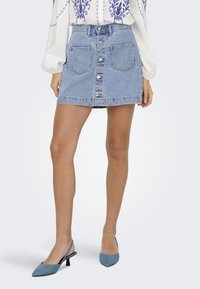 Denim skirt with a button-down front, two large front pockets, a light blue color, and a straight cut that ends above the knees.