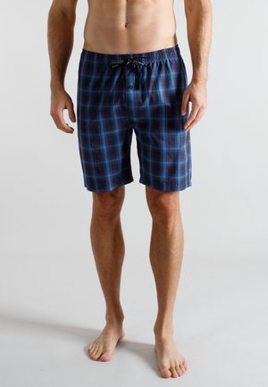 Man standing barefoot wearing blue and red plaid knee-length shorts with elastic waistband and drawstring.