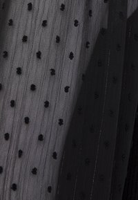 Tessuto nero trasparente con piccole palline in velluto sollevate e sottili righe verticali, che mostrano texture e riflesso della luce.