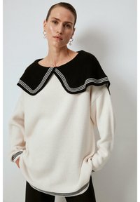 Maglione in maglia con una combinazione di colori in bianco e nero, colletto oversized a onde e cuciture decorative lungo i bordi. Vestibilità casual.