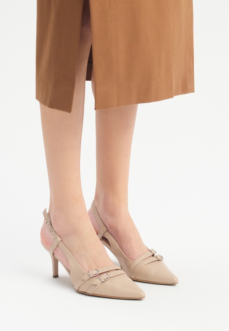 Scarpe slingback in pelle beige con punte appuntite, due sottili cinturini con fibbie argentate e tacchi di 7 cm. Texture liscia e design minimal.