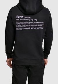 Felpa nera con cappuccio con testo viola sul retro. Il design include definizioni relative alla cultura hip-hop e all'uso dello slang.