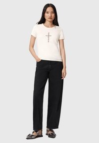 T-shirt crème à manches courtes avec un texte graphique sur le devant, associé à un jean large noir taille haute et des chaussures plates noires.