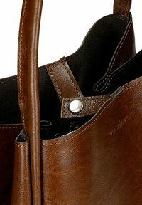 Brązowa skórzana torba na ramię o wyrazistym kształcie, z zapięciem na magnes i przeszyciem. Widoczna kieszeń wewnętrzna.