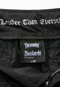 Svart jakkeinnside med "Louder Than Everything" og "Brandit Bastards" etiketter i hvit gotisk skrift. Størrelse M-lapp inkludert. Glatt tekstur.