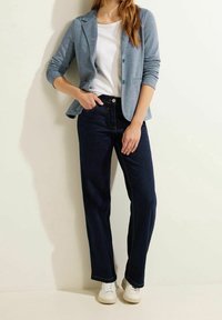 Lyseblå, tætsiddende blazer med to knapper, hvid t-shirt og mørkeblå jeans med lige ben. Hvide sneakers fuldender outfittet.