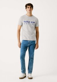 Grijze katoenen t-shirt met het "Red Bull Racing" logo in het blauw, gecombineerd met lichtblauwe jeans en witte sneakers met bruine zolen.