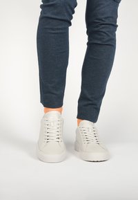 Zapatillas de cuero blanco con puntera redonda, suela de goma plana y seis ojetes para los cordones, combinadas con pantalones de corte tapered azul marino.