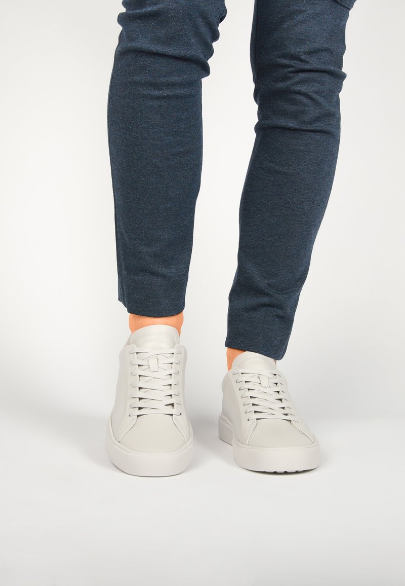 Zapatillas de cuero blanco con puntera redonda, suela de goma plana y seis ojetes para los cordones, combinadas con pantalones de corte tapered azul marino.