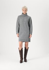 Robe en gris tricotée avec col roulé, dotée d'un motif en diamant texturé et d'un ourlet côtelé. Associée à des bottes de cow-boy marron jusqu'au genou.