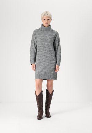 Robe en gris tricotée avec col roulé, dotée d'un motif en diamant texturé et d'un ourlet côtelé. Associée à des bottes de cow-boy marron jusqu'au genou.