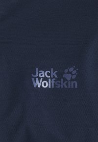 Tissu foncé avec le logo réfléchissant Jack Wolfskin et l'empreinte de patte imprimés au centre de la surface.