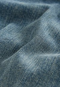 Tekstuuriga sinine denimpind, millel on nähtavad kudumise mustrid ja veidi kulunud pind. Pehme, paindlik ja sile puudutusele.