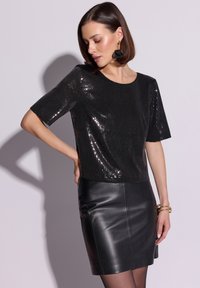 Czarna błyszcząca bluzka z cekinami, z krótkimi rękawami i okrągłym dekoltem, zestawiona z czarną skórzaną spódnicą o dopasowanym kroju i gładkiej fakturze.