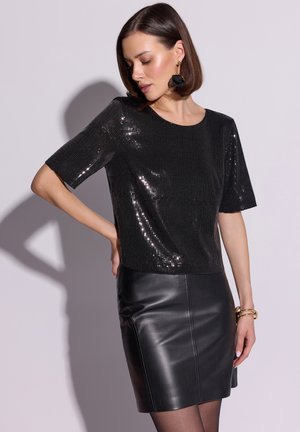 Czarna błyszcząca bluzka z cekinami, z krótkimi rękawami i okrągłym dekoltem, zestawiona z czarną skórzaną spódnicą o dopasowanym kroju i gładkiej fakturze.
