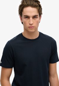 Mørkeblå bomulds T-shirt med klassisk rund halsdesign, korte ærmer og en lille logo detalje på venstre ærme. Blød tekstur.