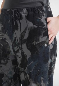 Mustat korkeavyötäröiset collegehousut, joissa on tummaharmaa ja sininen kukkakuosi, joustava vyötärönauha ja kiristysnyöri.