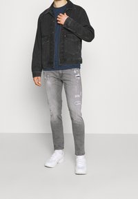 Svart denimjacka med två frampocket, kombinerad med en blå t-shirt och slitna ljusgrå jeans. Vita sneakers avslutar outfiten.