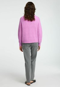 Rosa plüschiger Pullover mit lockerer Passform, rundem Ausschnitt und langen Ärmeln, kombiniert mit grauen geraden Jeans und schwarzen Ballerinas.