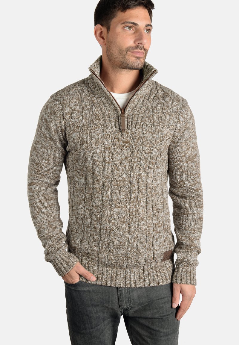 Brun kabelstrikket sweater med høj krave og lynlås, udstyret med ribbede manchetter og et struktureret mønster. Stoffet virker varmt og hyggeligt.