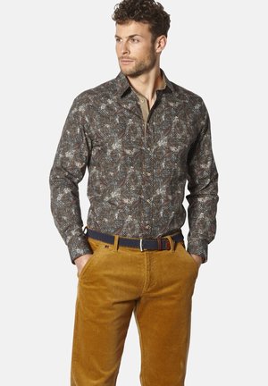 Langärmliges Shirt in Dunkelbraun mit geometrischem Muster; Knopfleiste, kontrastierender Kragen; kombiniert mit braunen Cordhosen und einem marineblauen Gürtel.