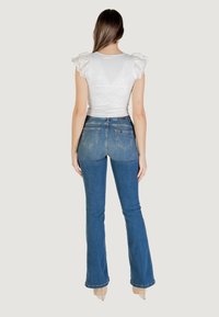 Top bianco a volant con finitura texturizzata abbinato a jeans blu a vita alta svasati, dotati di tasche posteriori e una silhouette aderente.