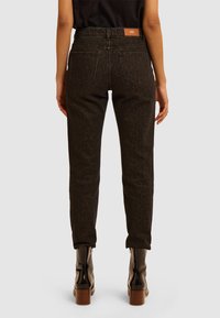 Jeans leopardati marroni con vita alta, gambe affusolate e design a cinque tasche. Presentano un'etichetta in pelle sulla cintura posteriore.