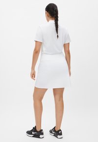 Hvid polo tshirt parret med en hvid skort, der har et figursyet design. Modellen bærer sorte sneakers med en hvid sål.