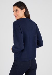 Maglione a maglia blu navy con maniche lunghe, scollatura rotonda e orlo leggermente corto e aderente. Texture morbida con dettagli a costine sui polsini.