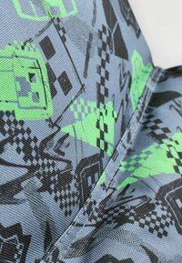 Tejido gris con un patrón pixelado que presenta elementos en negro y verde neón, incluyendo diseños que se asemejan a personajes y formas geométricas.