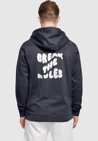 Marineblauer Hoodie mit einem großen, flauschigen weißen Schriftzug auf dem Rücken, der "BREAK THE RULES" lautet; mit einer Kapuze mit Kordelzug und gerippten Bündchen.