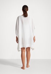 Balts lina kaftans ar brīvu piegriezumu, platām piedurknēm un izliekto apakšmalu. Tam ir vienkārša dekoltē līnija un viegla, gaisīga tekstūra.