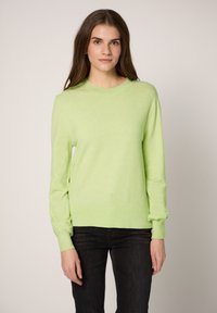 Maglione verde chiaro a maniche lunghe con collo rotondo e polsini a costine, realizzato in materiale morbido. Abbinato a jeans neri.